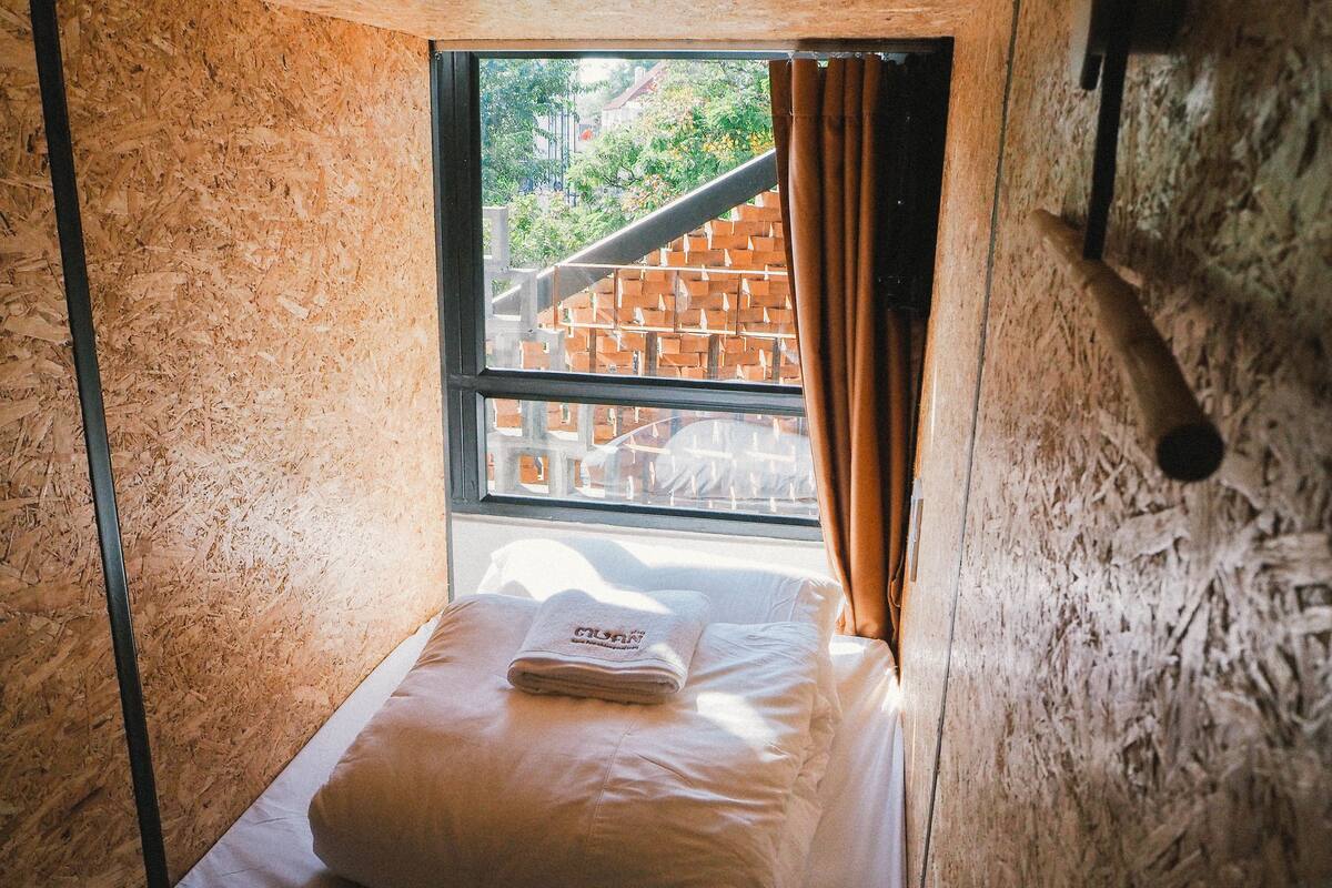 A small, single-bed room with a window overlooking a brick structure.