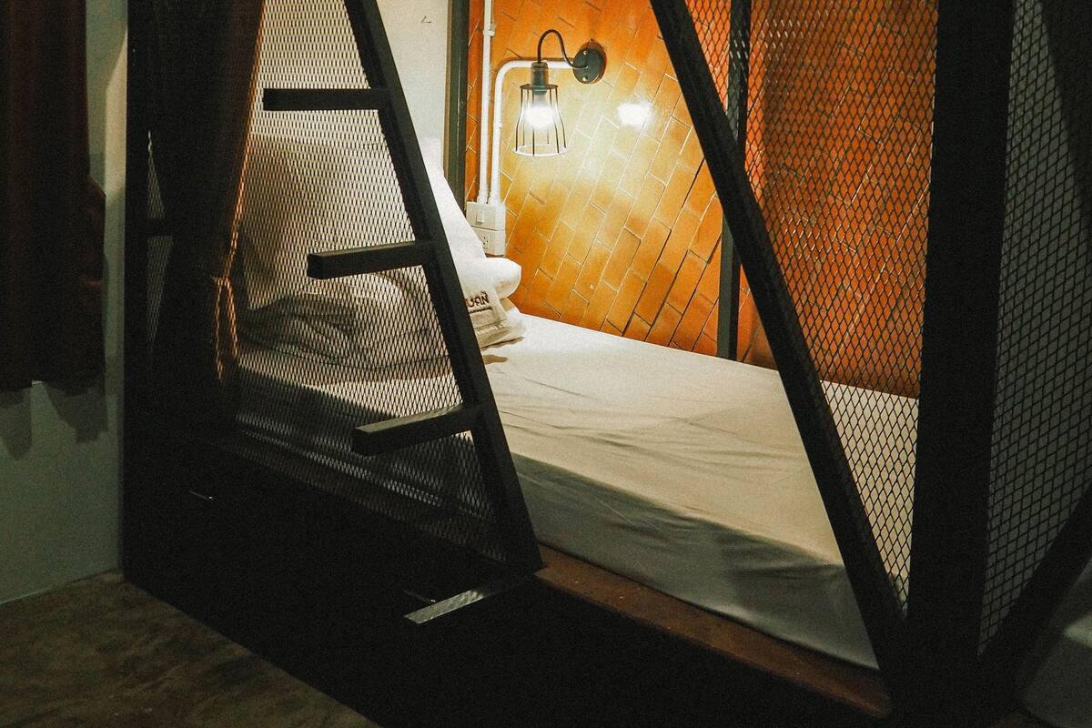 A bunk bed with a ladder, a small table, and a hanging light fixture.