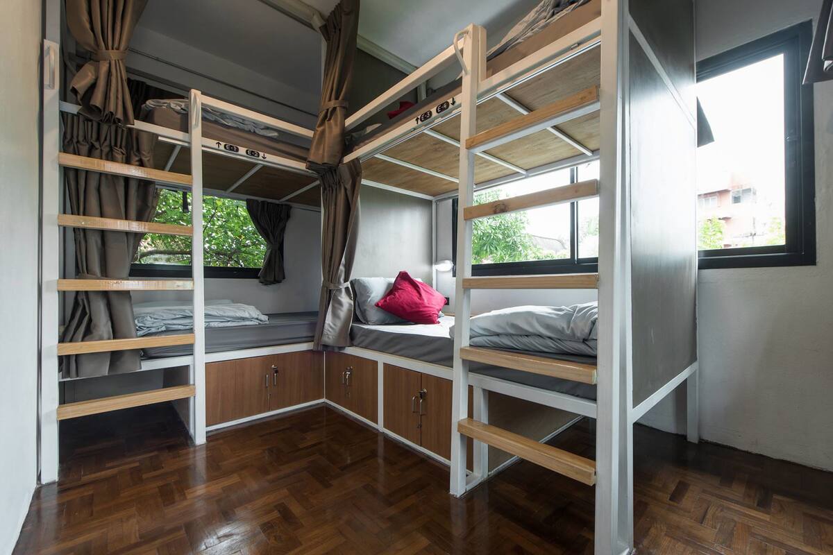 Habitación con literas, suelo de madera, ventana con cortinas y vista a la vegetación.