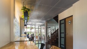 A spacious indoor area with a wooden table and chairs, a staircase, and a door with a sign. - Haus Hostel (Chiang Mai)