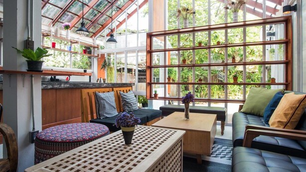 A spacious room with a large glass ceiling, wooden furniture, and potted plants. - Haus Hostel (Chiang Mai)