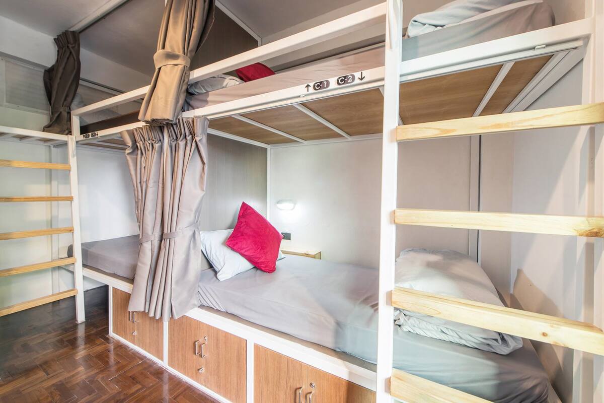 Habitación con literas de madera, una cortina y una almohada roja.