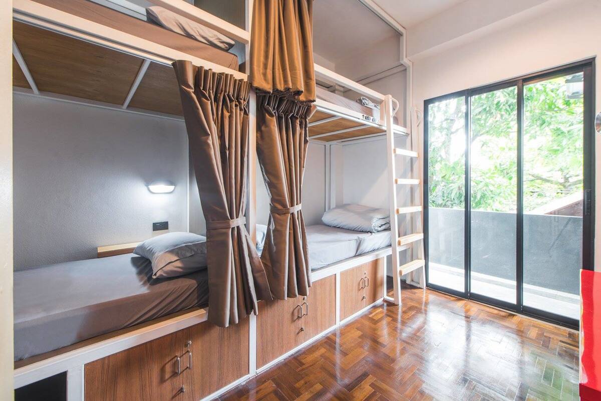 Una habitación compacta y moderna con literas, suelo de madera y un ventanal con vistas a zonas verdes.