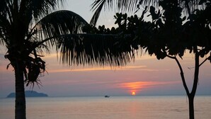 Un atardecer sobre un mar tranquilo con palmeras silueteadas contra el cielo.