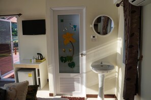 Una habitación con una puerta blanca decorada con un diseño floral, un lavamanos pequeño, un espejo redondo y un televisor montado en la pared.