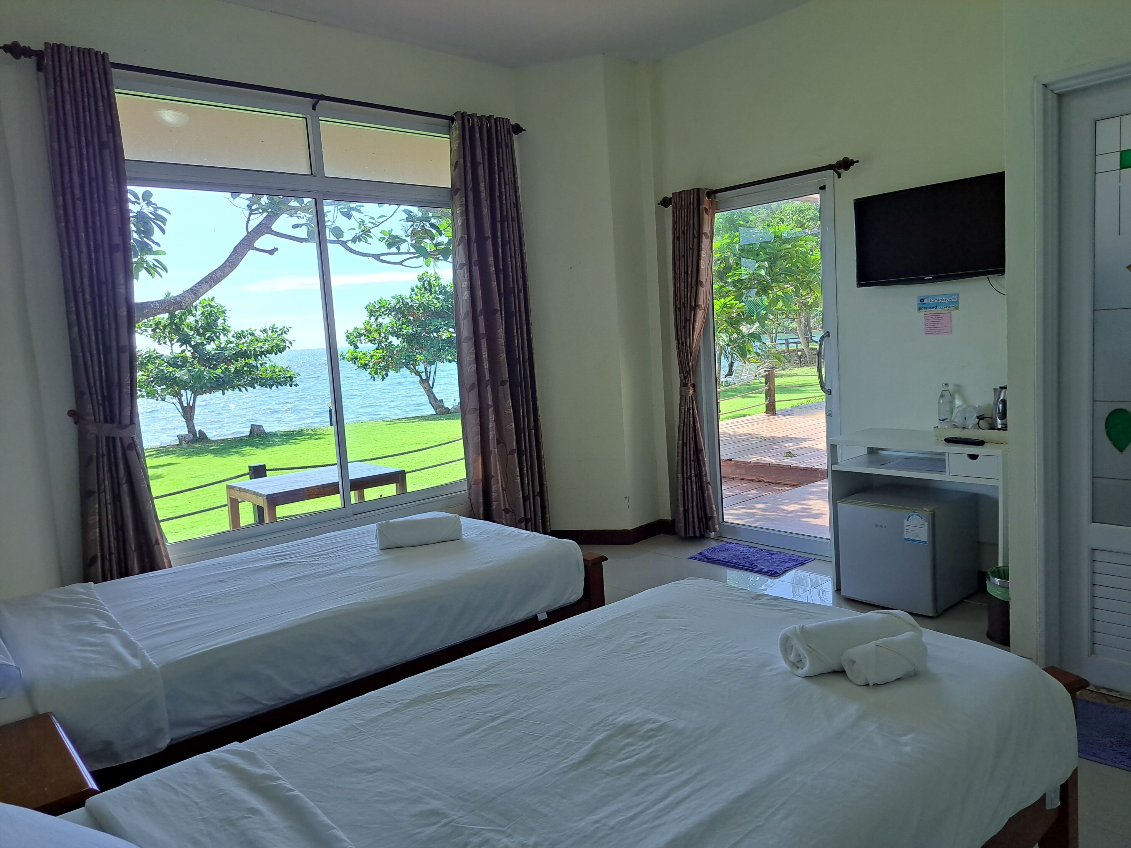 A hotel room with two beds, a television, and a view of the sea.