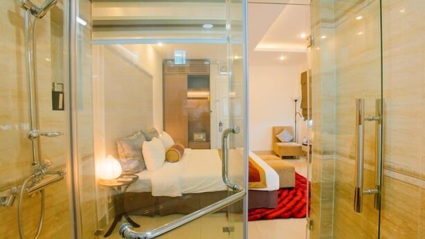 A modern hotel room with a glass shower enclosure, a bed with pillows and a blanket, and a small bedside table. - Smile Hotel (Hanoi)