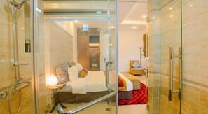 Une chambre d’hôtel moderne dotée d’une douche en verre, d’un lit avec des oreillers et une couverture, ainsi que d’une petite table de chevet.