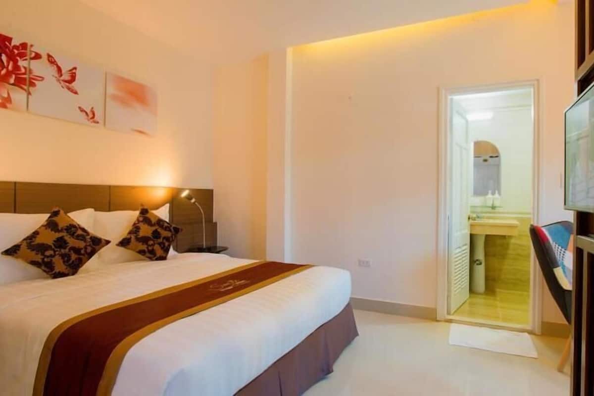 Una habitación de hotel con una cama, una mesita de noche, una lámpara, un cuadro en la pared y una puerta que da a un baño.