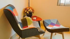 Two chairs with colorful patchwork upholstery, a small table with a vase of flowers, and a window in the background. - Smile Hotel (Hanoi)