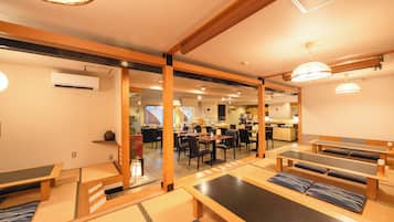 A traditional Japanese inn with tatami mat flooring, wooden furniture, and a kitchen area in the background.