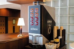 Une machine à café de la marque GEORGIA, dotée d’une interface numérique, d’un porte-tasse et d’un panier décoratif, le tout posé sur un comptoir en bois.