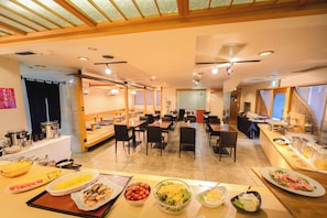 Un área de desayuno tipo buffet con diversas opciones de comida y diferentes disposiciones de mesas.