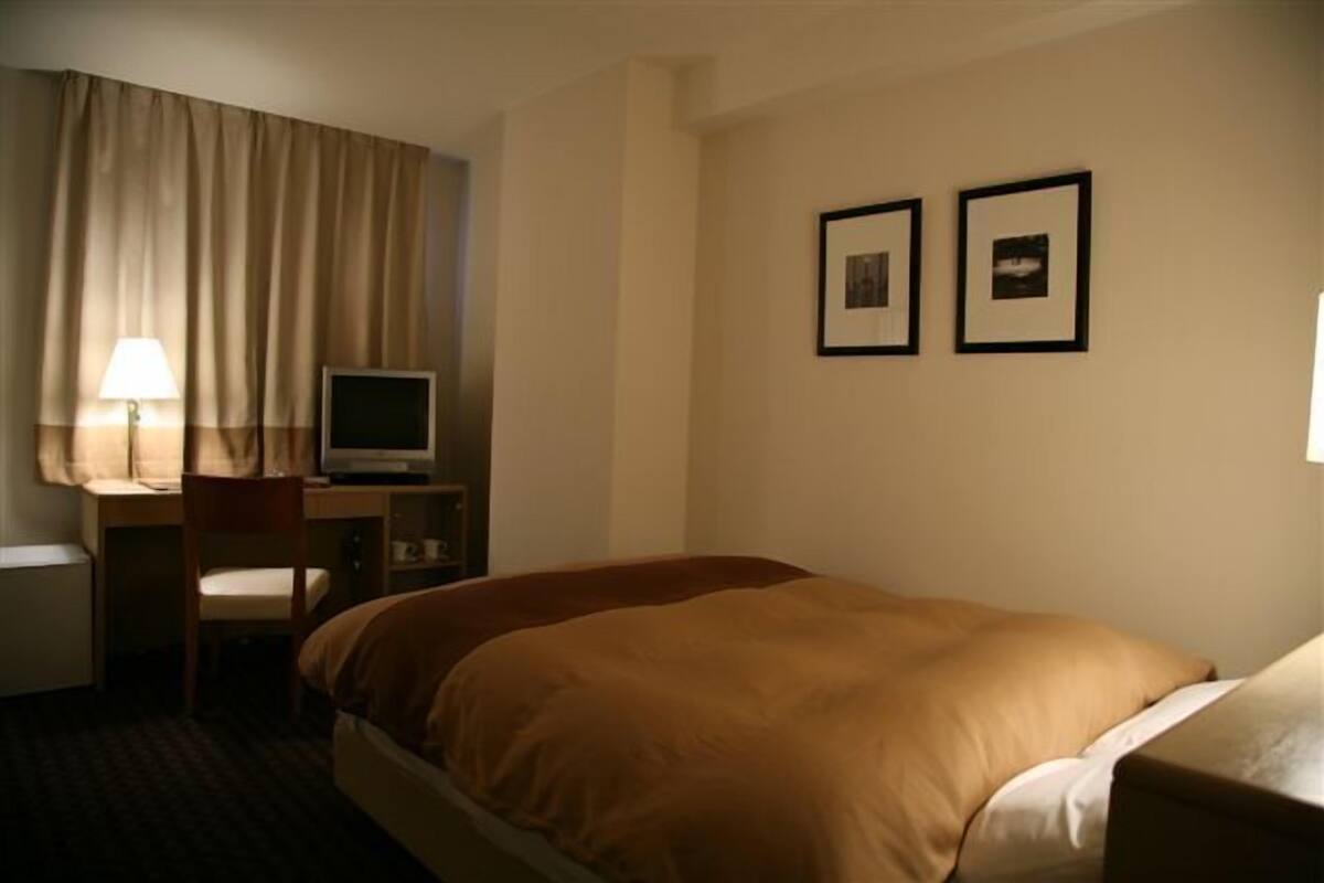 Ett hotellrum med en säng, ett skrivbord med en dator, en stol och två inramade tavlor på väggen.