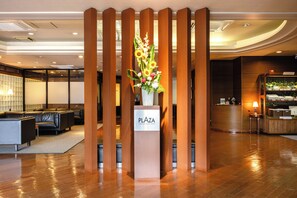 Un hall d’accueil d’hôtel avec un comptoir de réception en bois, un vase de fleurs et une enseigne indiquant « PLAZA HIROSAKI PLAZA HOTEL ».