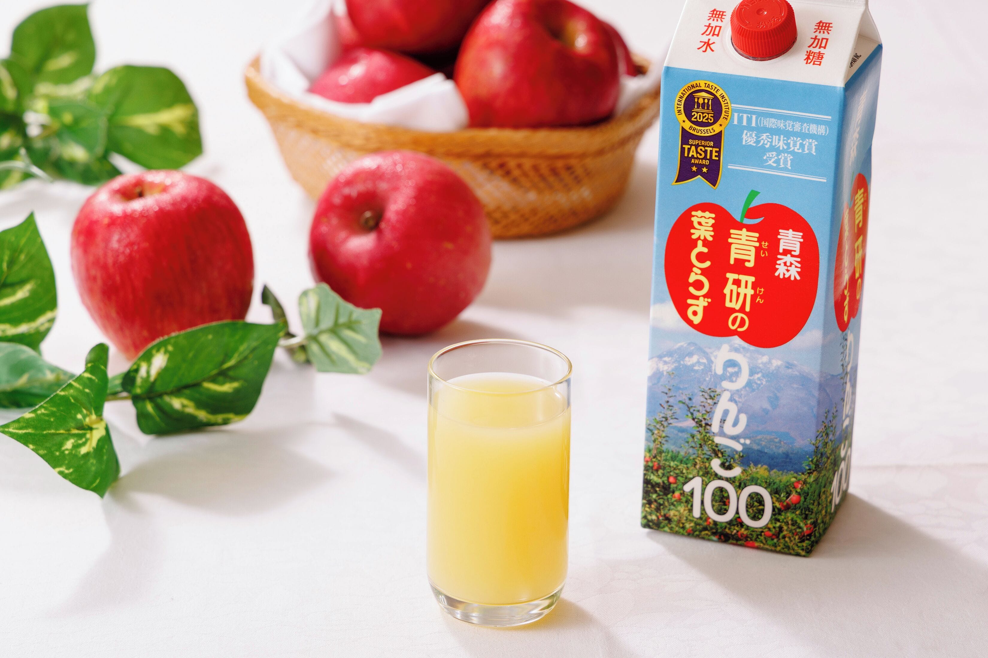 A carton of apple juice with a label, a glass of juice, and several apples.