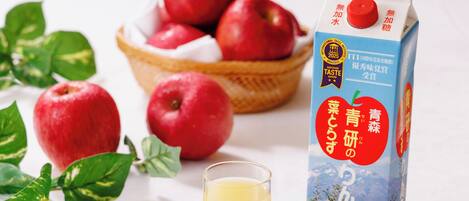 A carton of apple juice with a label, a glass of juice, and several apples.