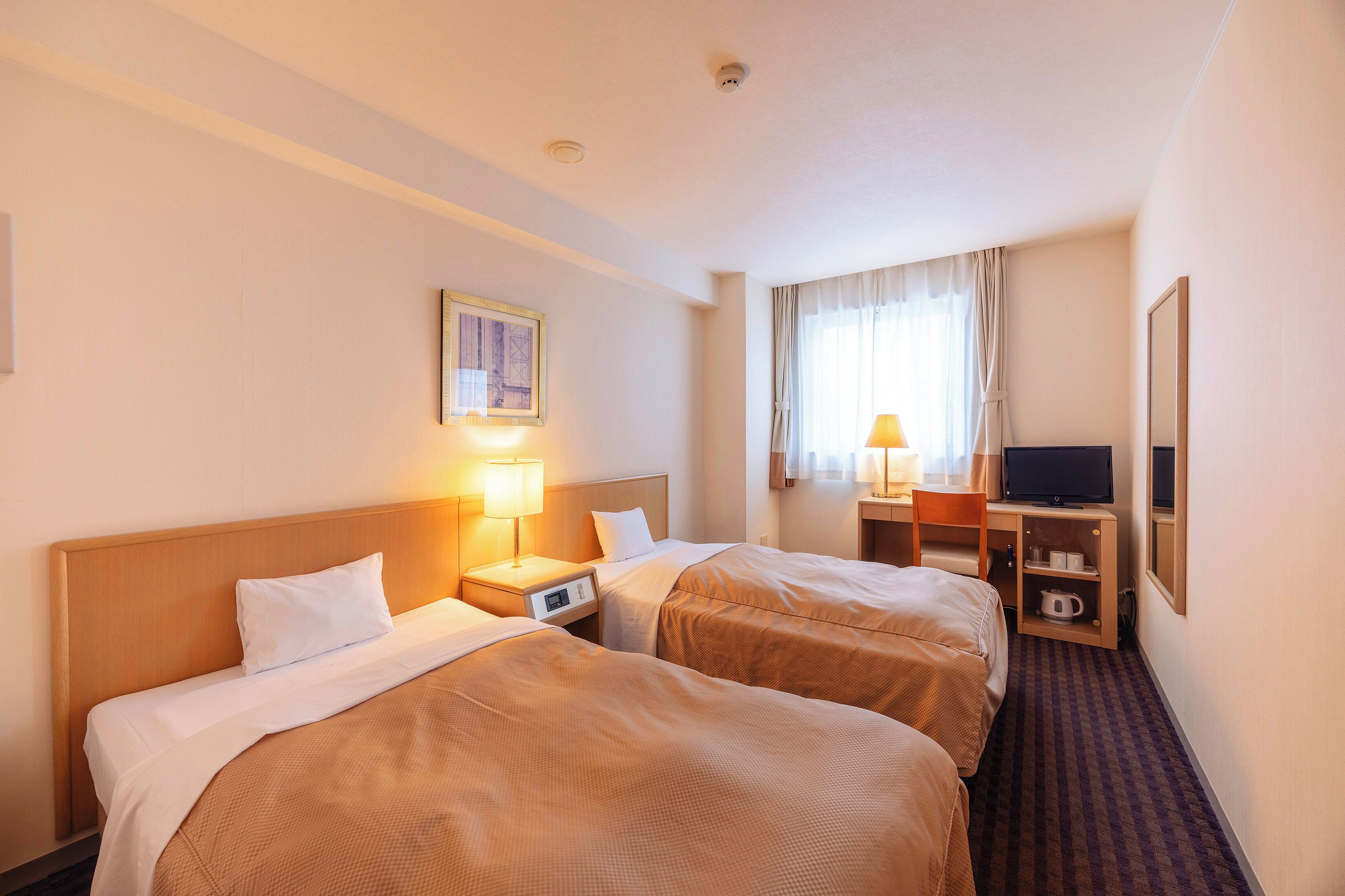A hotel room with two beds, a desk with a television, a window with curtains, and a painting on the wall.
