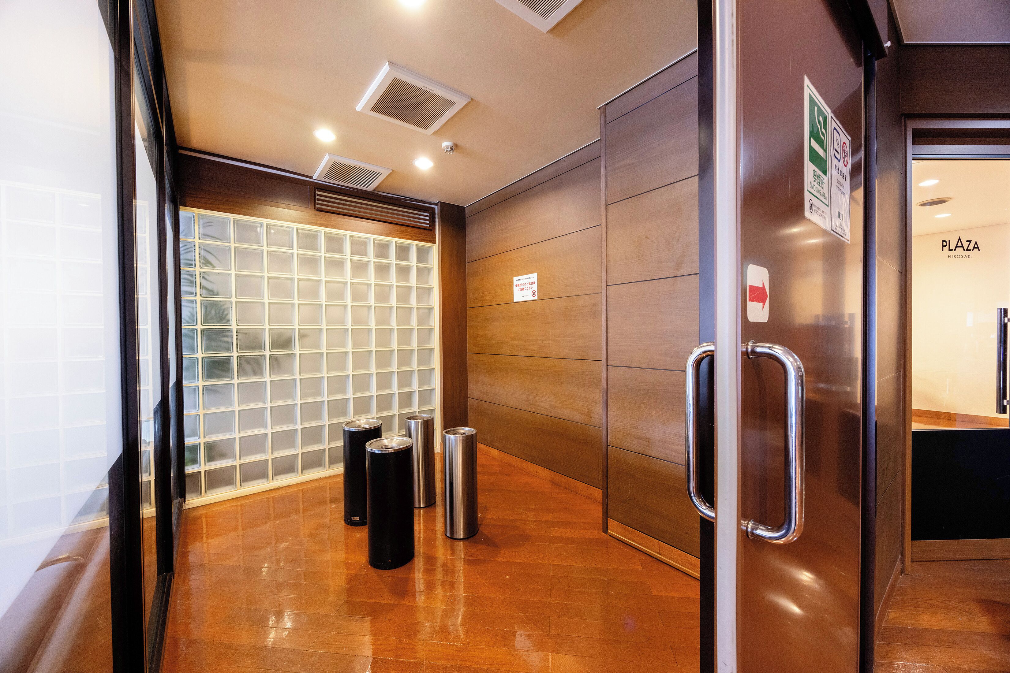 A modern elevator interior with a glass door, metal handrails, and a wooden wall panel.