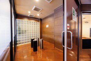A modern elevator interior with a glass door, metal handrails, and a wooden wall panel. - Hirosaki Plaza Hotel (Hirosaki)