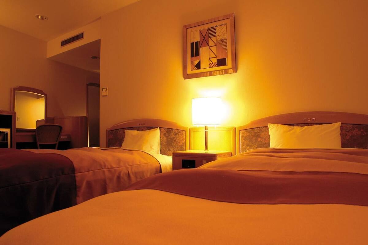 Ett hotellrum med två sängar, ett skrivbord med en stol, en spegel och ett konstverk som hänger på väggen.