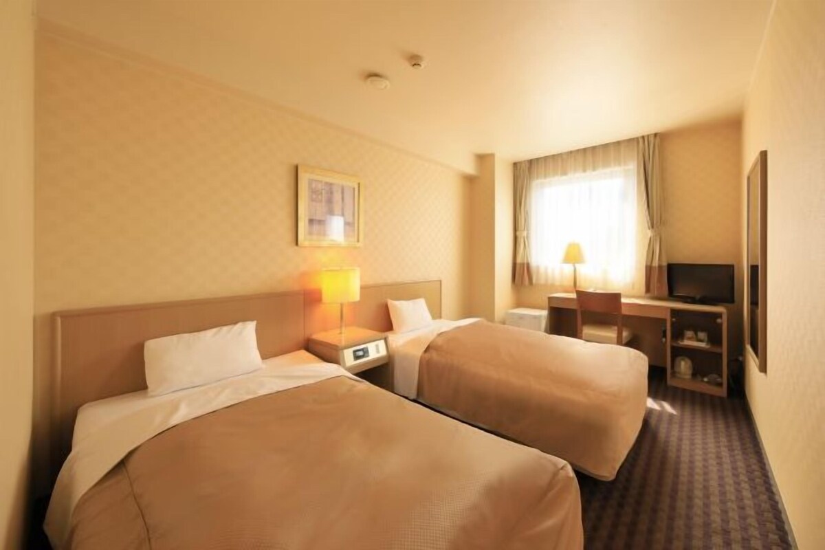 Een hotelkamer met twee bedden, een bureau, een televisie en een raam met gordijnen.