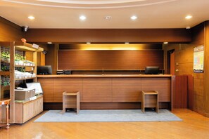 A modern reception area with a wooden counter, two stools, a security camera, and a sign on the wall. - Hirosaki Plaza Hotel (Hirosaki)