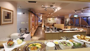 Un espace de restauration d’hôtel avec un buffet proposant divers plats, ainsi qu’un coin repas avec des tables et des chaises.
