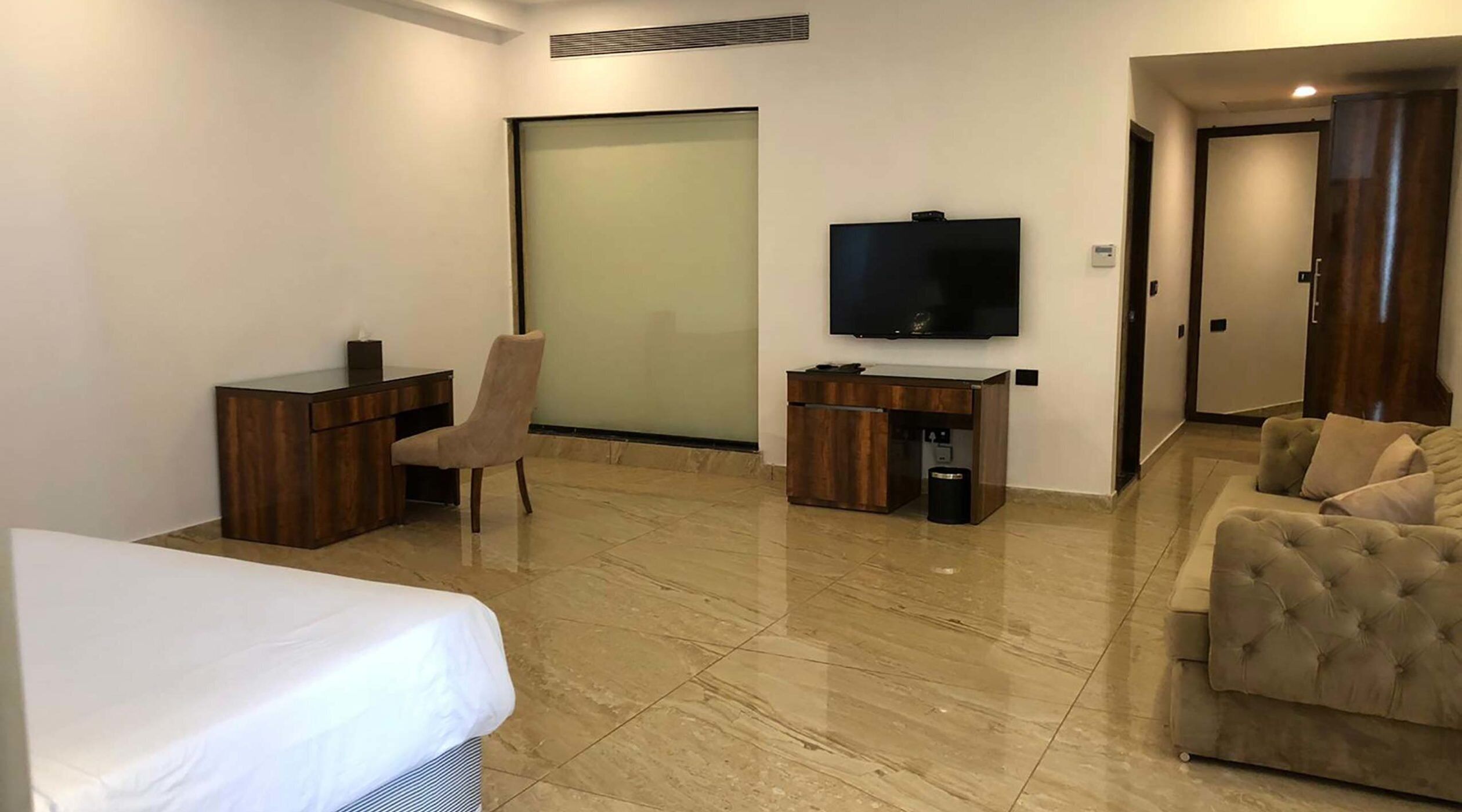 A hotel room with a bed, a desk, a chair, a TV, a sofa, and a sliding door.