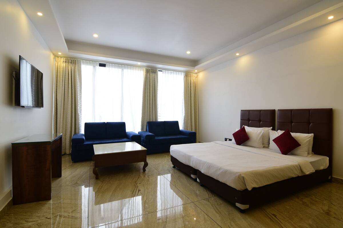 A hotel room with a bed, two sofas, a TV, and a desk.