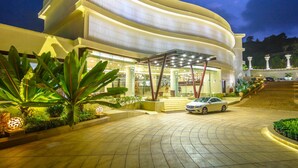 A modern hotel with a curved facade, a covered entrance, and a car parked in front. - Park Regis Goa (Arpora)