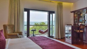 A hotel room with a bed, a chair, a small table, and a balcony with a view. - Park Regis Goa (Arpora)