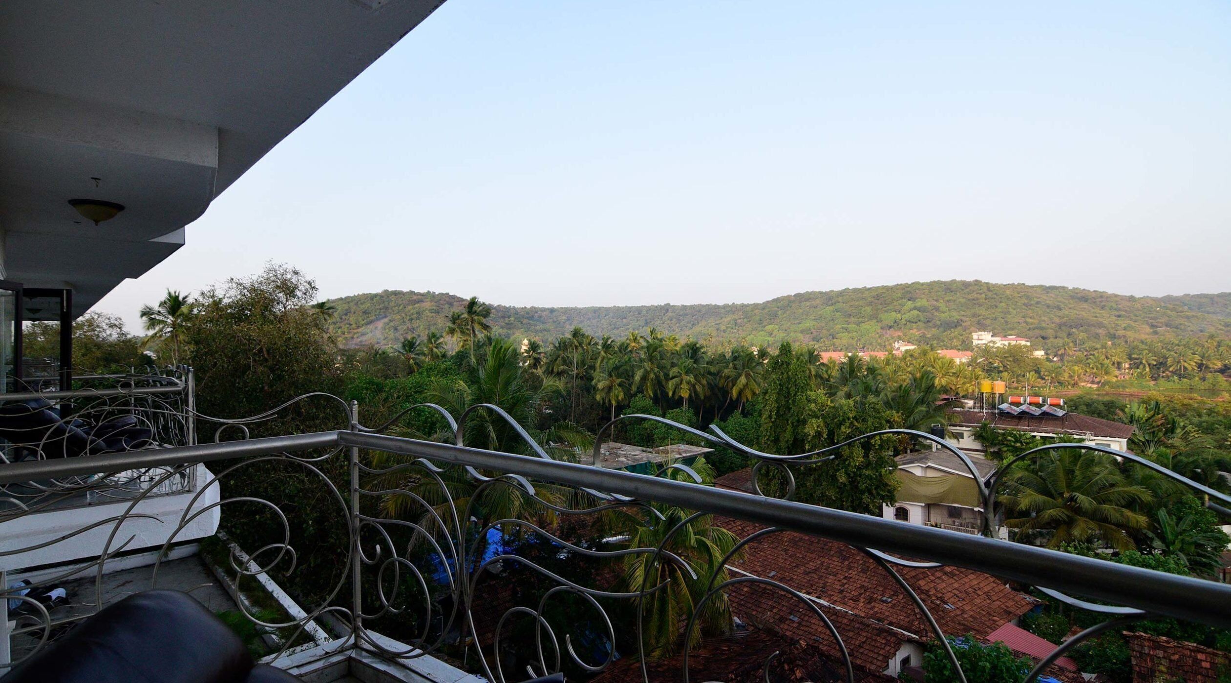 Un balcon offrant une vue sur un paysage vallonné, avec des palmiers et des bâtiments visibles au loin.