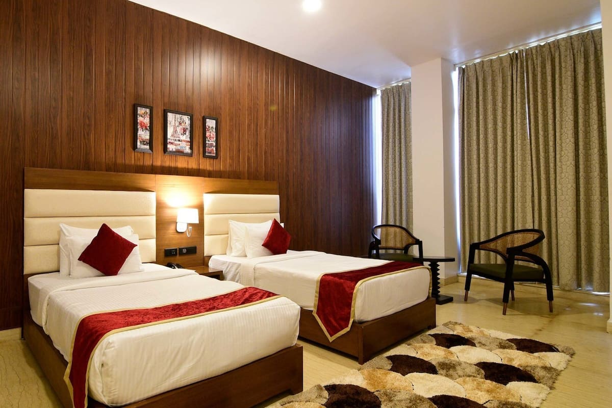 A hotel room with two beds, a wooden headboard, a small table, a chair, and a patterned rug.