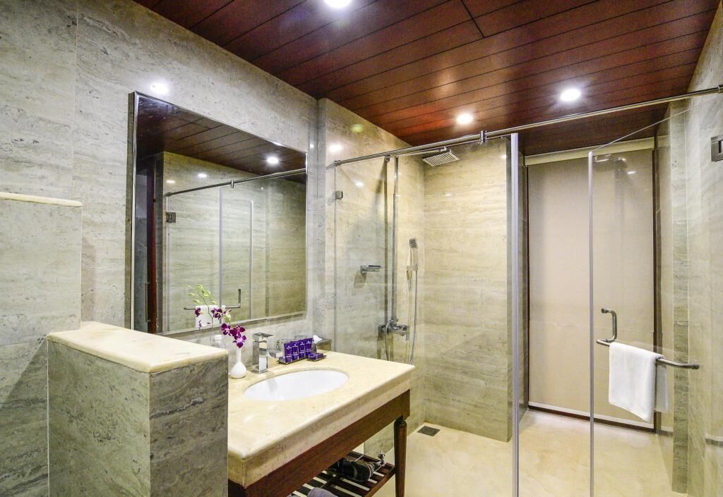 A modern bathroom with a marble vanity, a large mirror, a glass shower enclosure, and a wooden ceiling.