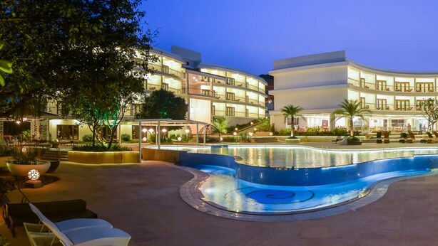 A hotel courtyard with a central pool, outdoor seating, and a multi-story building with balconies. - Park Regis Goa (Arpora)