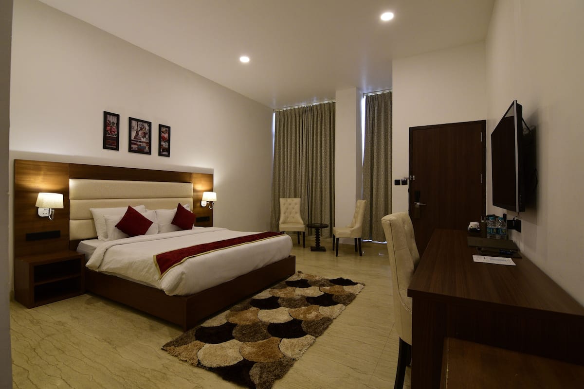 A hotel room with a large bed, bedside tables, a desk, a chair, a TV, and a window with curtains.
