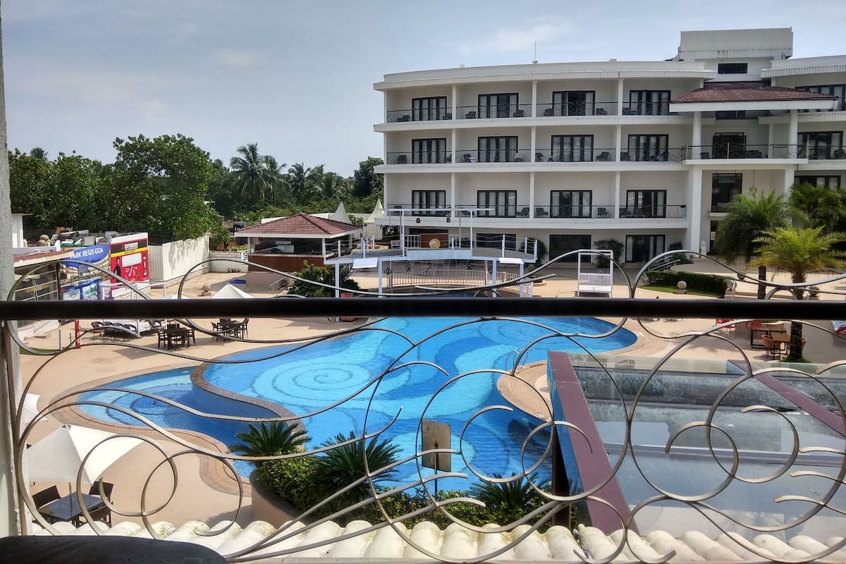 A hotel with a swimming pool, multiple balconies, and a view of a nearby restaurant.