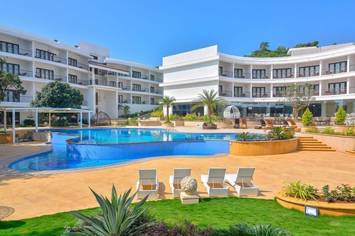 A modern hotel with a large pool, outdoor seating, and a well-maintained garden.