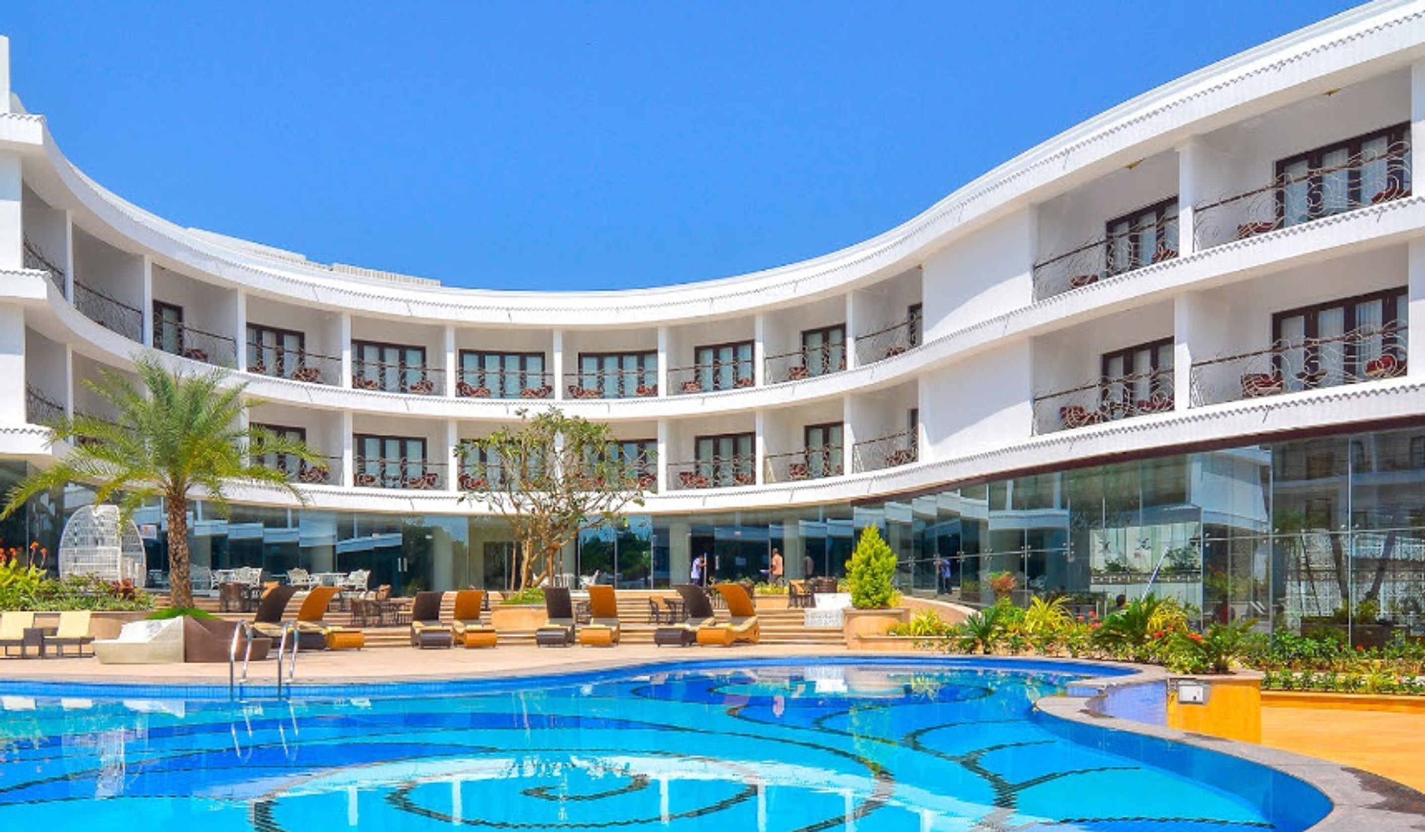 Ein mehrstöckiges Hotel mit einem zentral gelegenen Schwimmbad, Sitzgelegenheiten im Freien und Balkonen mit Geländern.