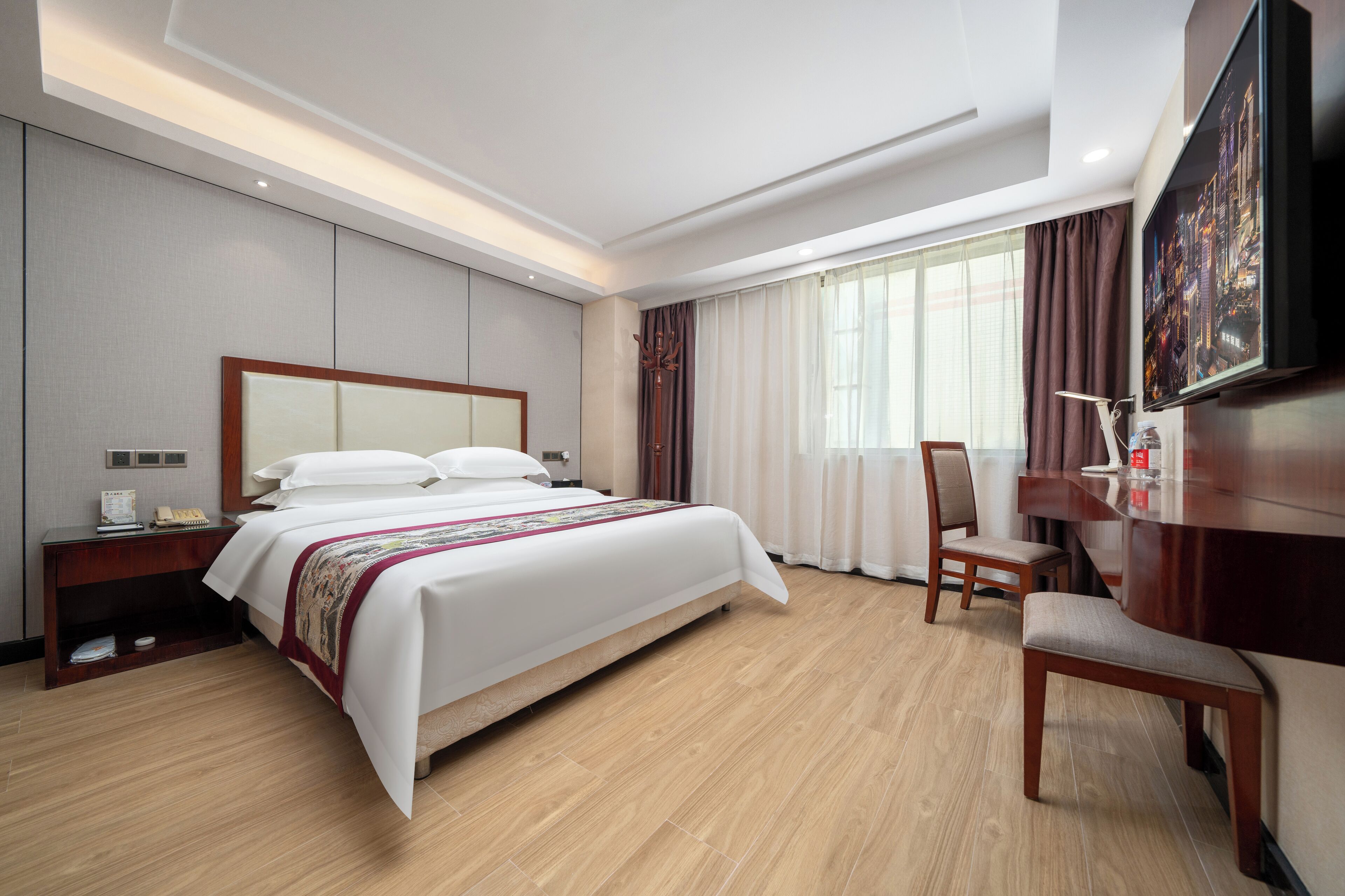 A hotel room with a large bed, a desk, a chair, and a television.