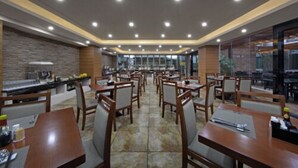 Un restaurante amplio con numerosas mesas y sillas, una barra con menú y vistas a través de amplios ventanales.