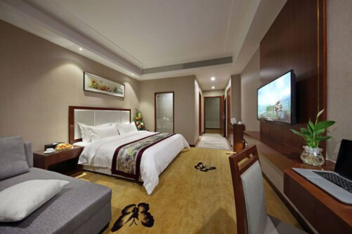 Quarto de hotel com cama, escrivaninha com laptop, televisão e sofá.
