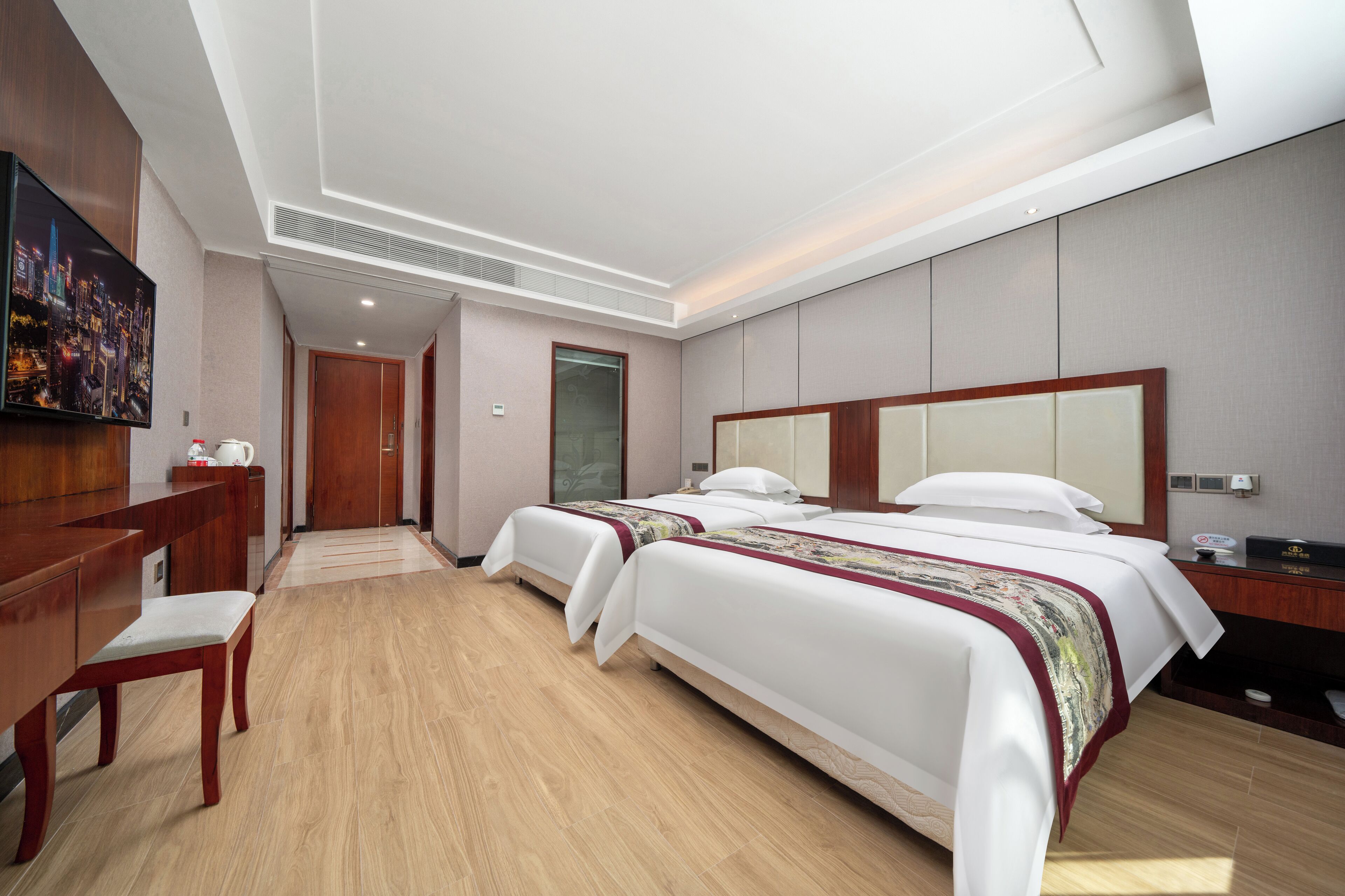 A hotel room with two beds, a desk, a chair, a television, and a large mirror.