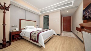 Una habitación de hotel con una cama grande, un perchero de madera, una mesita de noche con teléfono y un televisor montado en la pared.