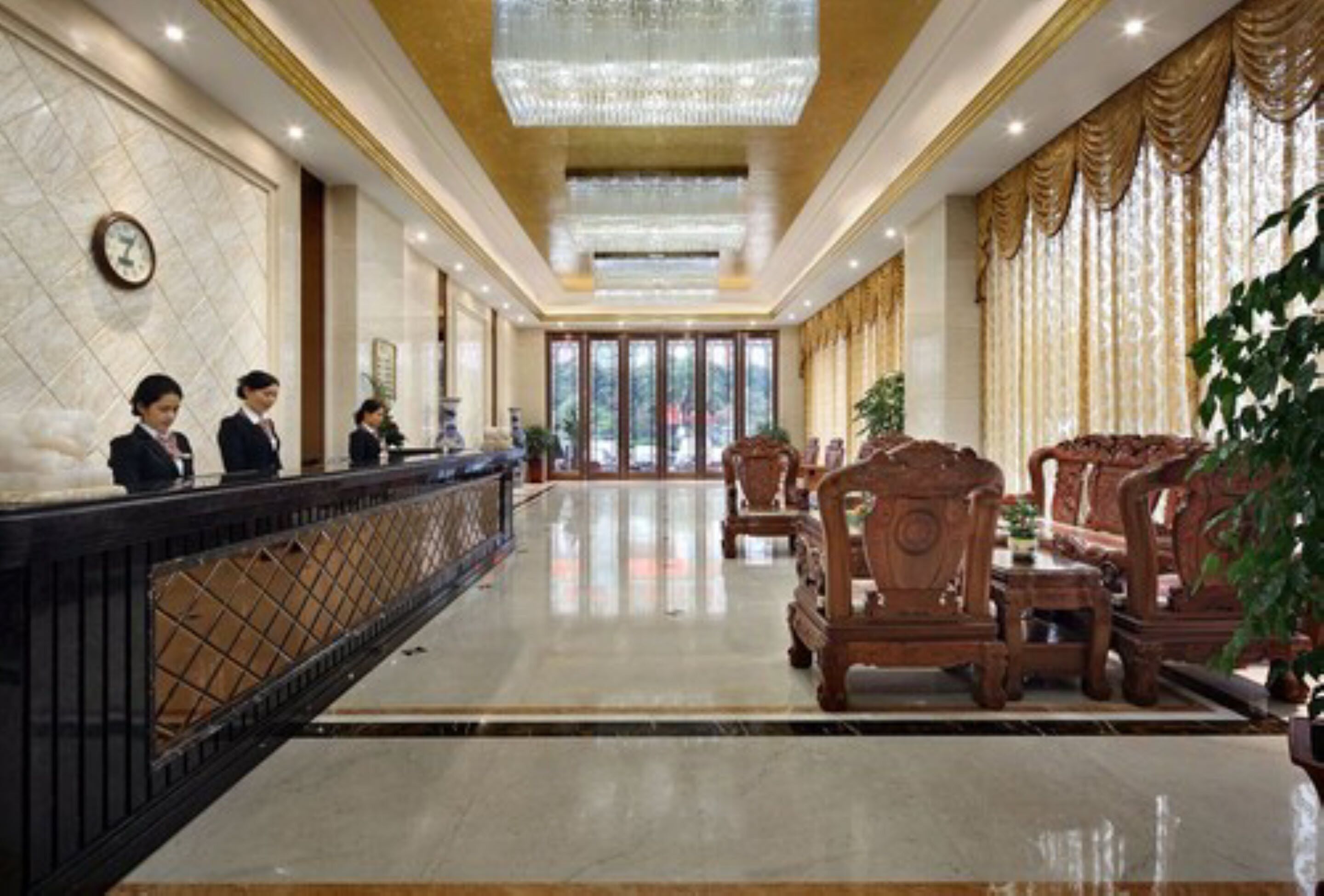 A hotel lobby with a reception desk, wooden chairs, and a chandelier.