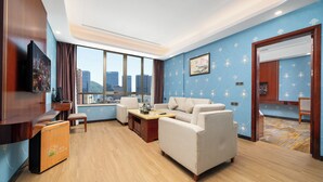 Una sala de estar moderna con un sofá, una mesa de centro y un televisor. Hay un ventanal con vistas a la ciudad, y las paredes son azules con un estampado floral.