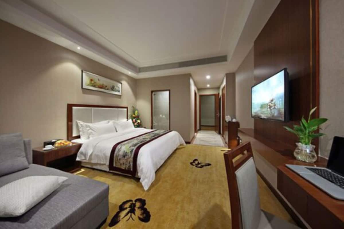 Quarto de hotel com cama, escrivaninha com laptop, televisão e sofá.