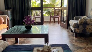 Una habitación con una cama, una mesa de vidrio con una flor púrpura, un control remoto y un sillón estampado.
