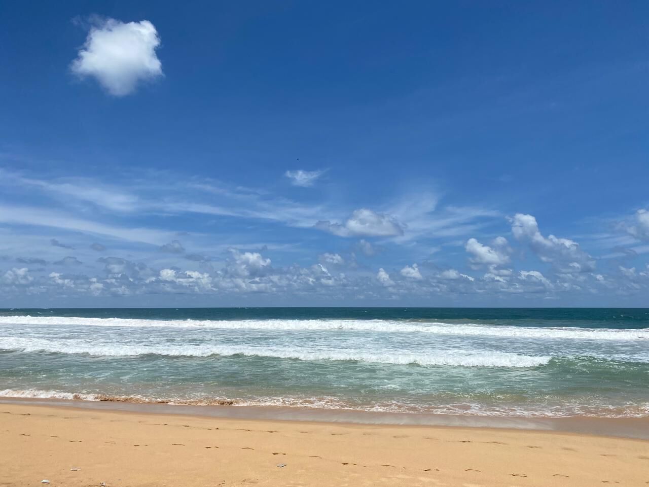 Une plage avec des vagues, un ciel dégagé et quelques nuages.